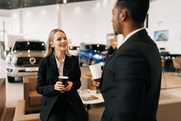 Rear view of relaxed multiethnic business people in formal outfit having break after meeting, talking during drinking coffee together in auto dealership. Concept for lifestyle of businesspeople.