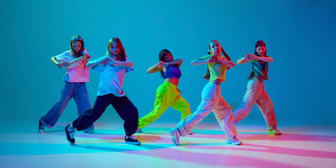 Energetic, artistic young girls in motion, performing hip hop dance against cyan blue background in...