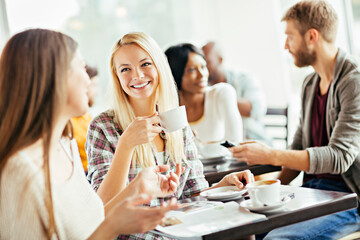 Diverse young friends drinking coffee in busy cafe