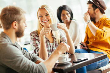 Diverse young friends drinking coffee in busy cafe