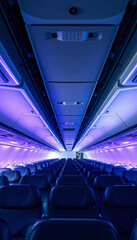 Fototapeta premium An airplane interior with rows of blue seats and overhead compartments, illuminated by blue and purple lighting