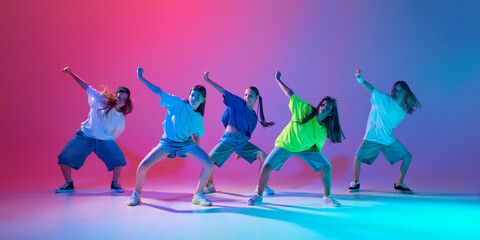 Children perform a high-energy hip hop dance, showing skills of synchronization against gradient pink purple background in neon light. Concept of modern dance styles, youth culture, active lifestyle