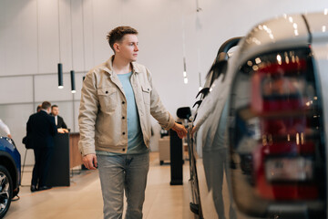 Male buyer looking around big open trunk of car in motor show. Male customer choosing pickup truck...