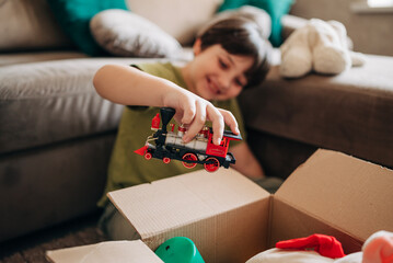 Happy cheerful kid boy packing his toys for delivery donation box. Charity and recycling