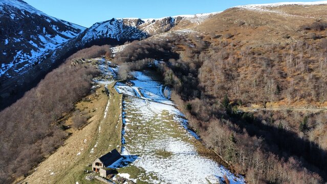  This stunning image captures a natural landscape from an aerial perspective. It features a winding river partially covered with snow, surrounded by rolling hills and sparse vegetation. 