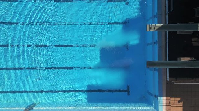 Aerial view of an empty swimming pool with diving platforms, showcasing clear blue water and serene surroundings. Perfect for sports, architecture, and recreation-themed projects