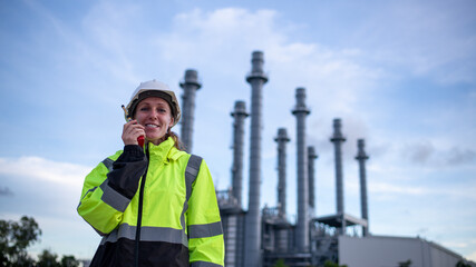 Engineers wearing safety gear, including hard hats examining survey a large blueprint tablet standing industrial facility gas or oil refinery engaged in a job requires high safety standards concept.