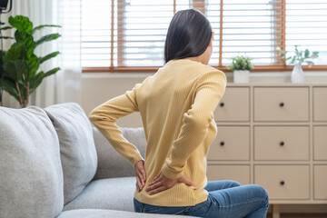 Close-up woman massaging her lower back has back pain because of sitting posture during work in...