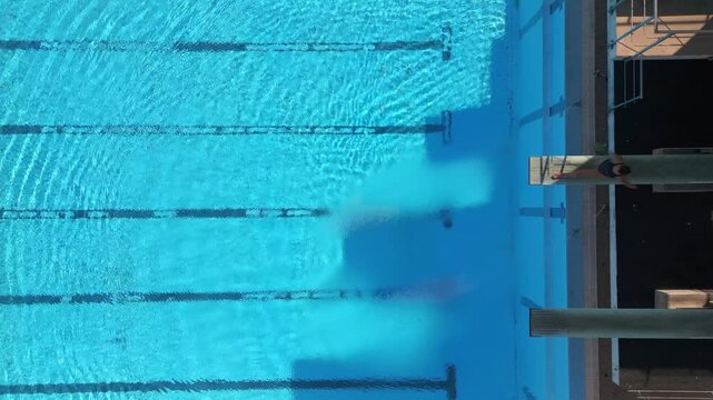 Drone footage capturing a diver mid-air performing a tuck dive above a clear blue pool, with stunning reflections and precise timing. Perfect for sports, aerial, and aquatic-themed projects