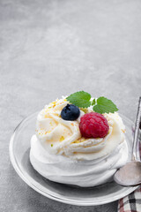Mini Pavlova meringue nest with berries and whipped cream on gray background