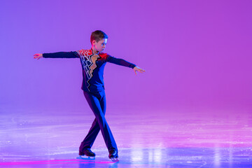 Boy figure skater skating on ice. With festive colored lilac lighting.