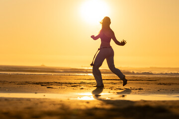 Woman practicing capoeira martial arts at sunset on the beach