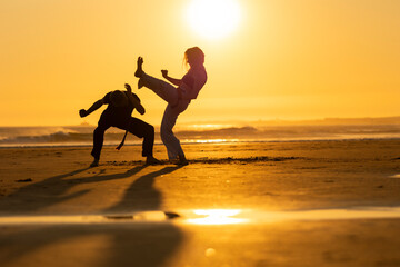 Fototapeta premium Two people practicing capoeira martial arts on the beach at sunset