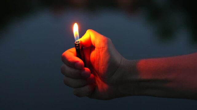 The flame from the lighter burns close-up.
A man's hand holds a lighter.
Man with a lighter at night