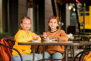 Two schoolgirls are sitting at a table in a city open-air cafe.