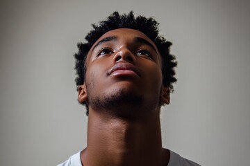 Obraz premium Young man with an upward gaze his face illuminated by soft light representing hope ambition and the drive for self improvement in a modern minimalist setting