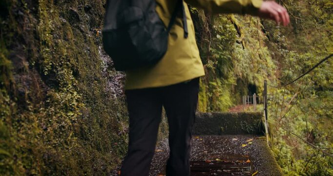 Female hiker trekking on wet levada trail through waterfalls on Levada irrigation canal on Madeira Island