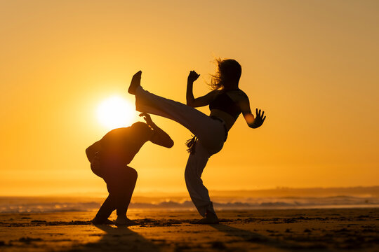 Couple practicing capoeira martial art at sunset on the beach