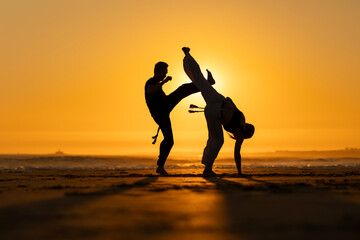 Two people practicing capoeira martial arts at sunset on the beach