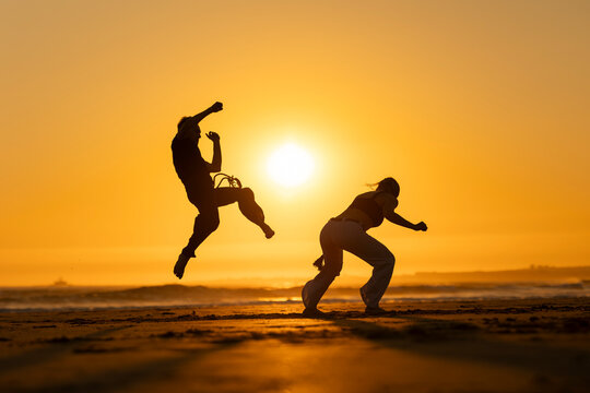 Couple practicing capoeira martial art at sunset on the beach