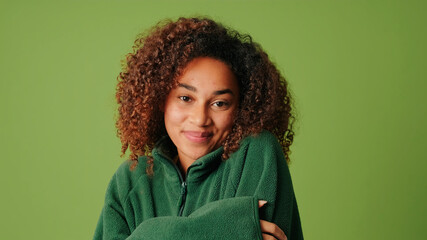 Melted positive dark skinned woman with afro hairstyle keeps hands on cheeks and feels happiness isolated over green studio background