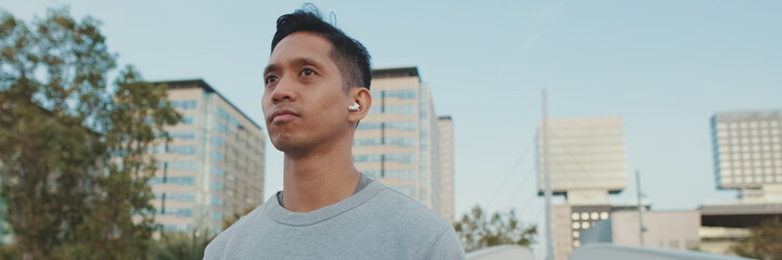 Athlete in wireless headphones, a guy in sportswear, walks along the bridge, panorama