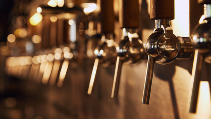 Row of shiny beer taps with wooden handles, set against blurred background with warm lighting. Cozy pub atmosphere. Concept of beer, brewery, pub, Oktoberfest, traditions