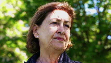 Contemplative Elderly woman in a park, smiling softly with sunlight highlighting her hair. The vibrant green foliage in the background