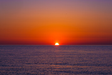 The sun is sinking below the horizon over the sea