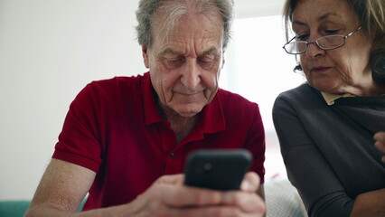 Elderly couple focused on smartphones, exploring apps together, engaged in modern technology, digital literacy, senior lifestyle, bonding over gadgets, casual indoor setting, learning new skills