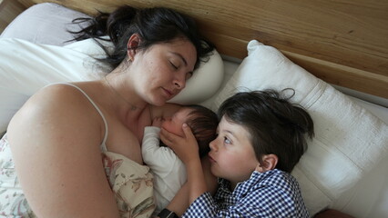 Mother holding newborn baby with young son beside her, tender family bonding, morning routine, cozy home atmosphere, maternal love and care, peaceful and intimate moment, nurturing touch