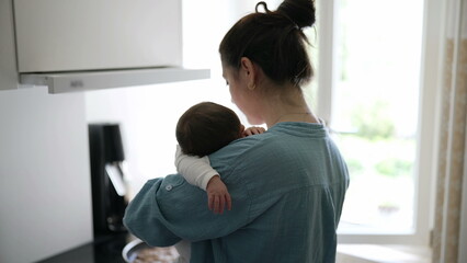 Obraz premium Mother multi-tasking in the kitchen, holding her baby while focusing on cooking, natural light streaming through the window, delicate balance of nurturing and daily chores