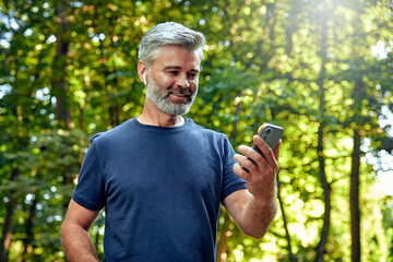 An active man is jogging in the beautiful nature while using his smartphone device