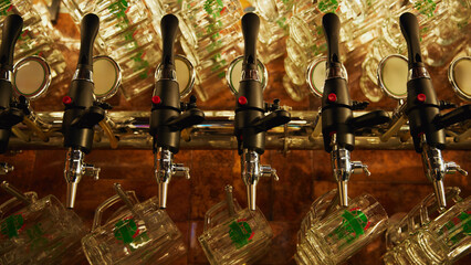 Row of shiny beer taps with handles, set against wall with rows of empty mugs hanging from it. Vintage and luxury atmosphere. Concept of beer, brewery, pub, Oktoberfest, traditions