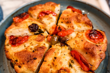 close up of Italian Focaccia Barese with tomato, ham cut into six pieces on a blue plate