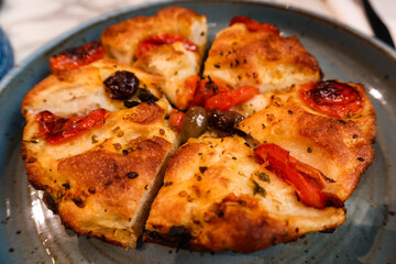 close up of Italian Focaccia Barese with tomato, ham cut into six pieces on a blue plate