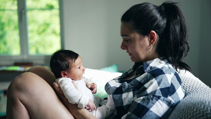 Obraz premium Mother holding newborn baby in her arms, both looking at each other with love and tenderness, indoor setting with soft natural light coming through the window, close-up of their faces, emotional bond