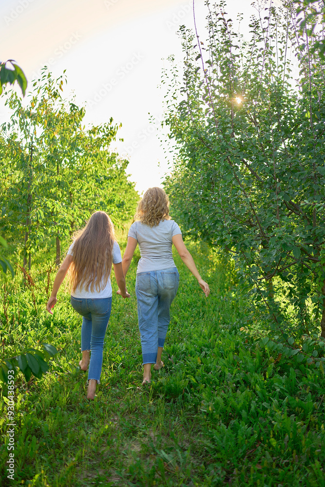 Wall mural mother and teenage girls with long blond hair spend time together in the sunlit park