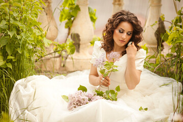 THE EUROPEAN BEAUTIFUL BRIDE WITH THE BEAUTIFUL DARK HAIR WITH THE BOUQUET ON THE BACKGROUND OF THE GREAT BRUSH OF LILAC