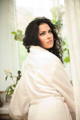a cute smiling girl in a white robe rests on a bed early in the morning