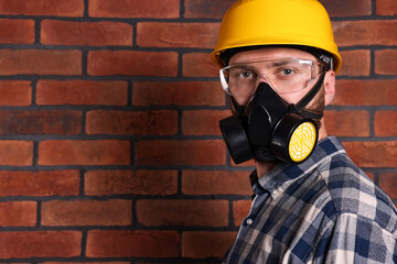 Man in respirator mask and hard hat near red brick wall. Space for text