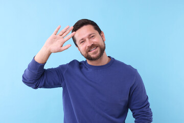 Naklejka premium Cheerful man waving on light blue background