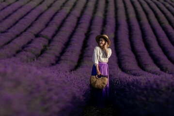 A woman stands in a field of lavender flowers, wearing a straw hat