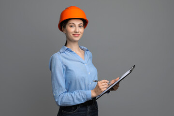 Engineer in hard hat with clipboard and pen on grey background