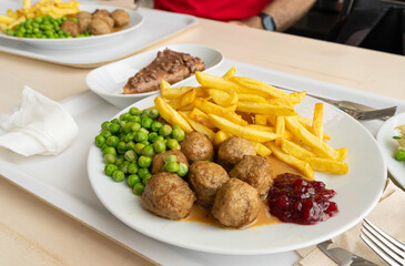 Meatballs with french fries, green peas, bechamel sauce and cranberry jam, meat balls on white plate