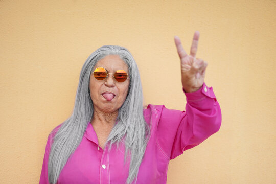 Grazy granny doing peace gesture with thonge out wearing trendy hippie glasses - Cool elderly woman portrait - Focus on the face