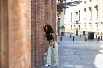 beautiful latin woman with black eyes and dark, long curly hair rests her head on an arm leaning against a brick wall. The woman is happy on holiday in Seville, Spain.