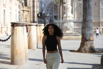 beautiful young latin woman with dark eyes and long curly hair walks through the centre of Seville, in the background you can see the cathedral of catholic worship and gothic style of Seville, Spain.