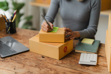 Small Business Owner Writing Shipping Label: A close-up view of a small business owner's hands meticulously writing a shipping label on a cardboard box, showcasing the dedication and personal touch in
