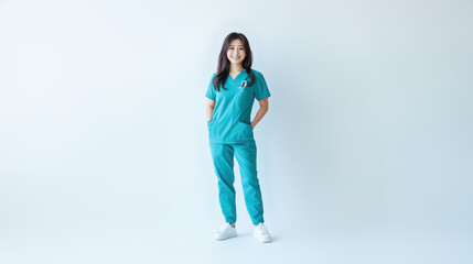 Fototapeta premium A young Asian nurse radiates positivity in teal scrubs, smiling with her hand in her pocket while looking at the camera against a white background.
